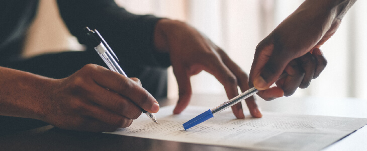 two peoples hands reviewing a contract with pens in their hands and paper on the table breach of contract