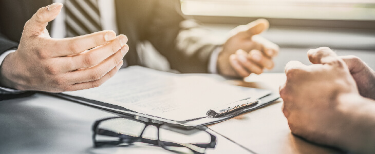 mans hands over a clipboard with glasses on the table and hands across from them commercial litigation