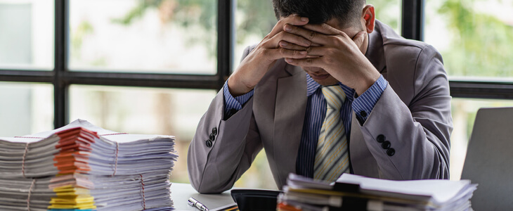 Stressed businessman sitting on his desk with piles of documents surrounding him