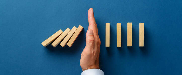 View from above of male hand interfering collapsing dominos in a conceptual image of business crisis management. Over navy blue background.