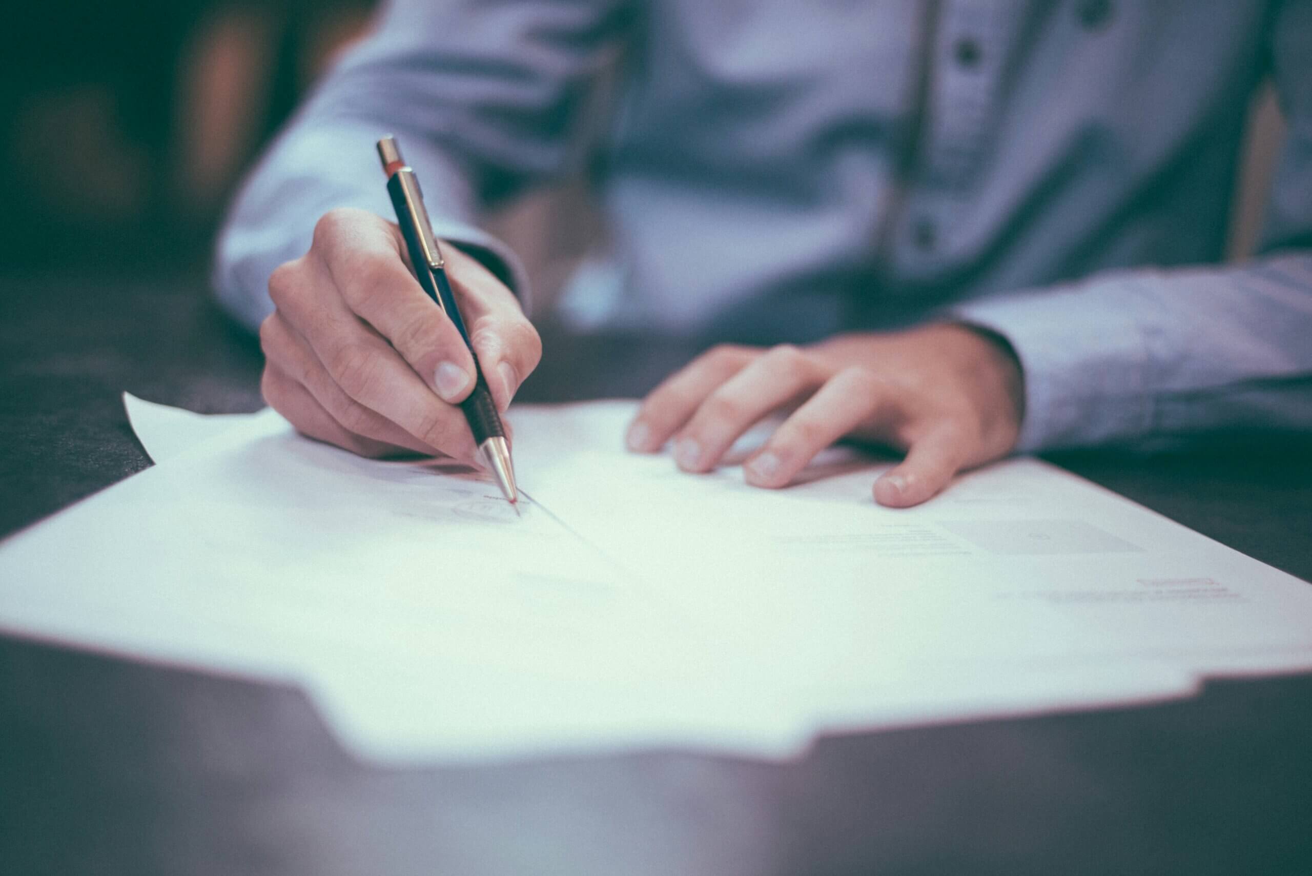 Close-up of hands writing on legal papers with a pen