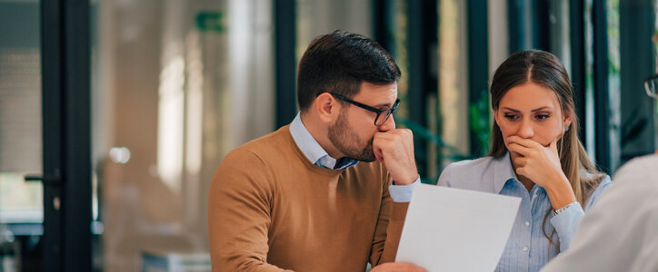 Portrait of a couple with financial problems looking at document in financial adviser's office.