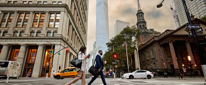 Full length side view of Black woman and bearded Hispanic man in 20s and 30s on their way home after work, One World Trade Center in background.