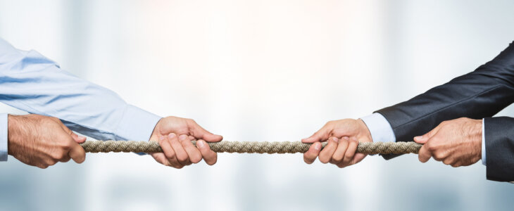 Tug of war, two businessman pulling a rope in opposite directions over defocused background with copy space