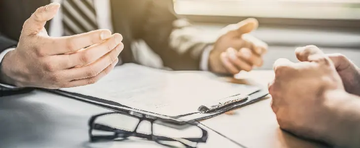 mans hands over a clipboard with glasses on the table and hands across from them commercial litigation