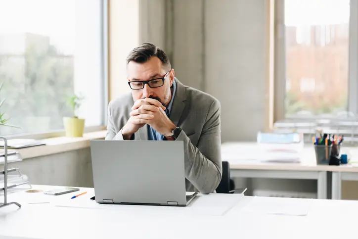 Thoughtful middle aged handsome businessman in shirt working on laptop computer in office. Man working in office