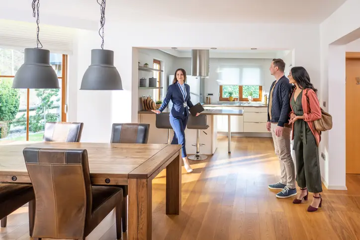 Young female real estate agent showing couple modern kitchen and dining room in apartment