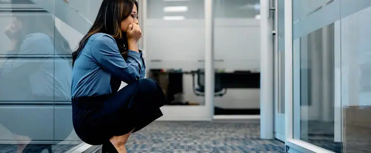 Stressed out Asian business woman, crouching in hallway on an office building. Copy space.
