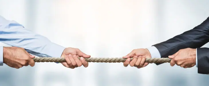 Tug of war, two businessman pulling a rope in opposite directions over defocused background with copy space