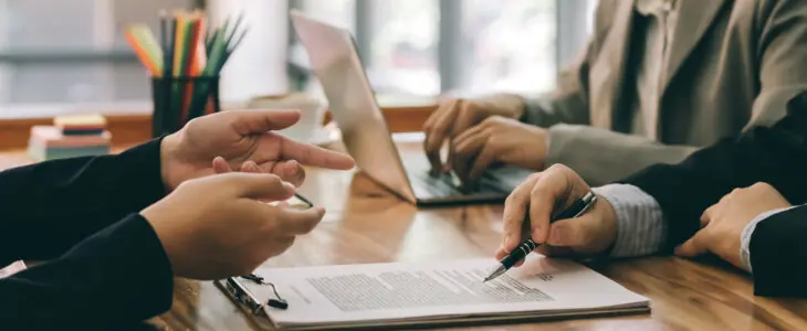 Close-up of professionals reviewing and discussing a document on a clipboard at a meeting table.